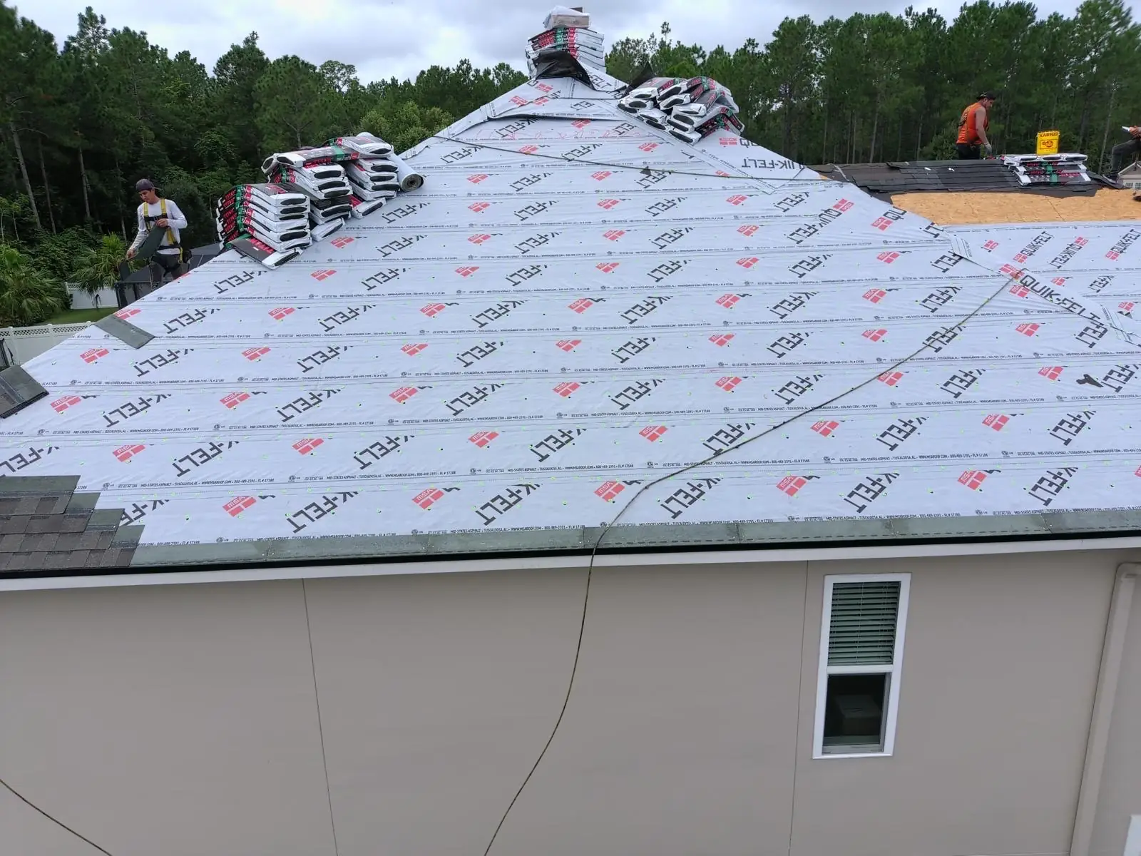 Roof covered in gray synthetic underlayment with bundles of shingles staged at the ridge