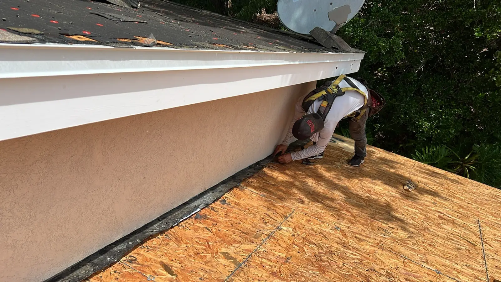 Roofer in a safety harness fitting new decking against a stucco wall