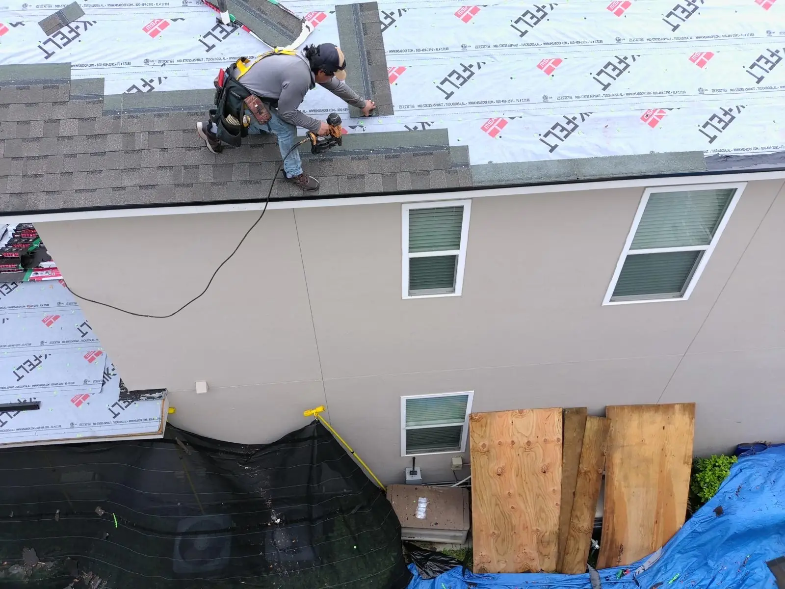 Aerial view of a roofer nailing architectural shingles over fresh underlayment