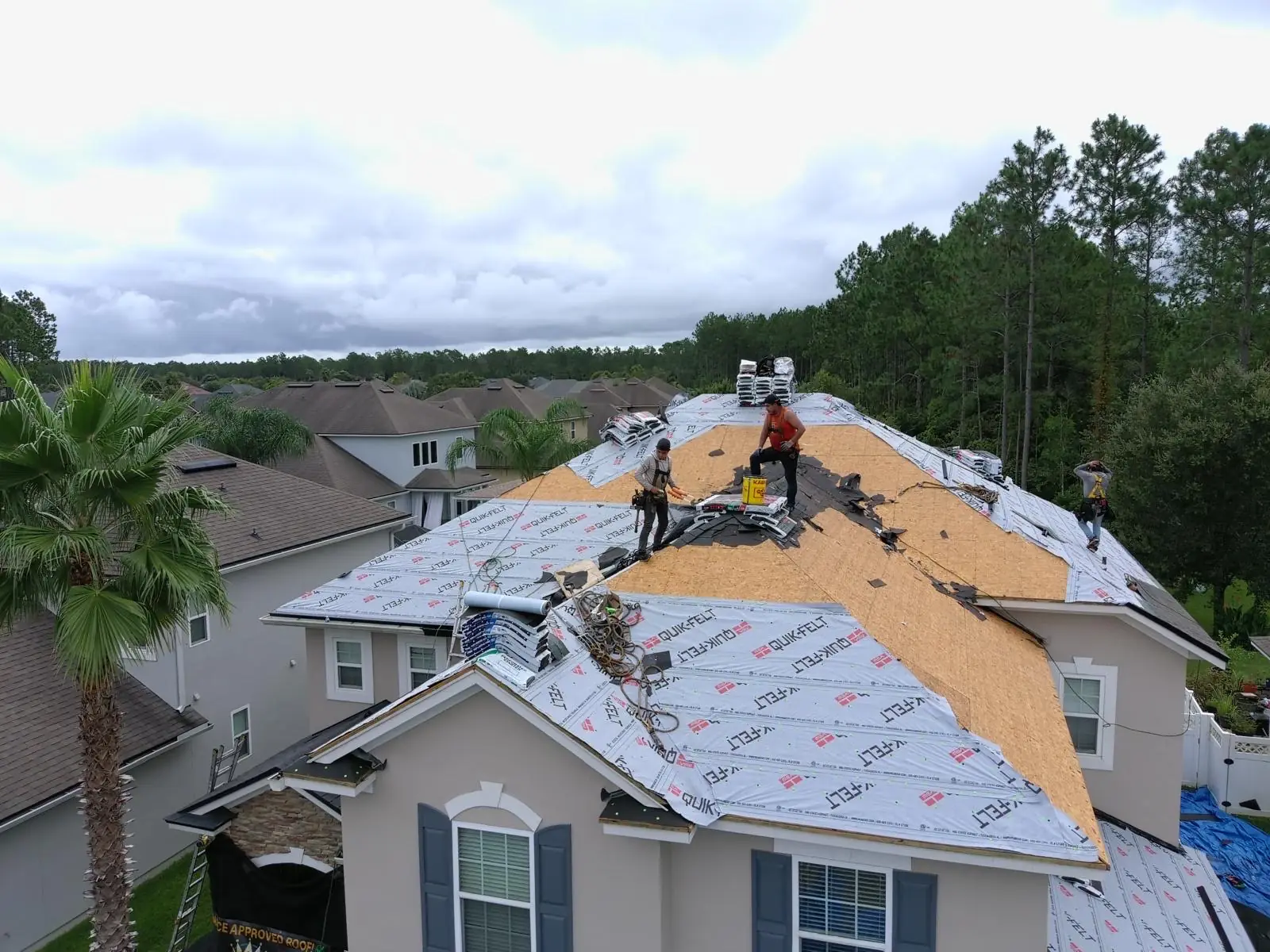 Aerial view of a two-story home with new underlayment installed, crew on the ridge