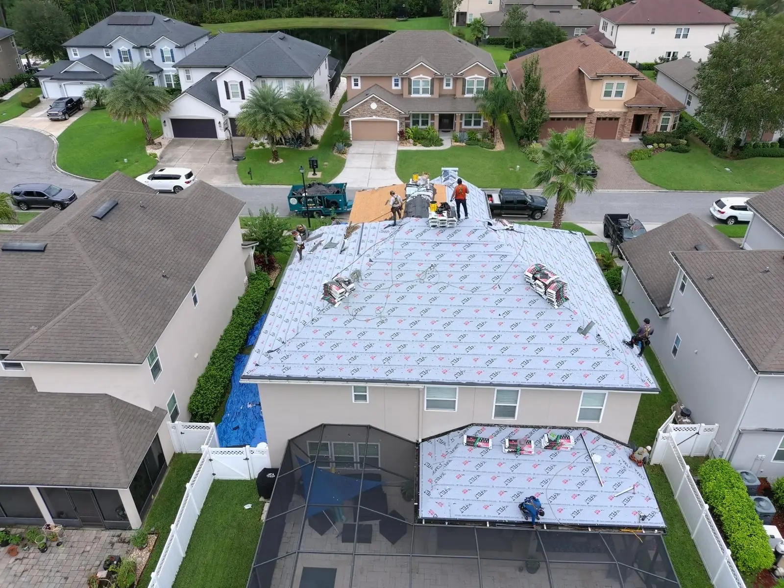Aerial view of a crew installing synthetic underlayment on a two-story home in a Northeast Florida neighborhood
