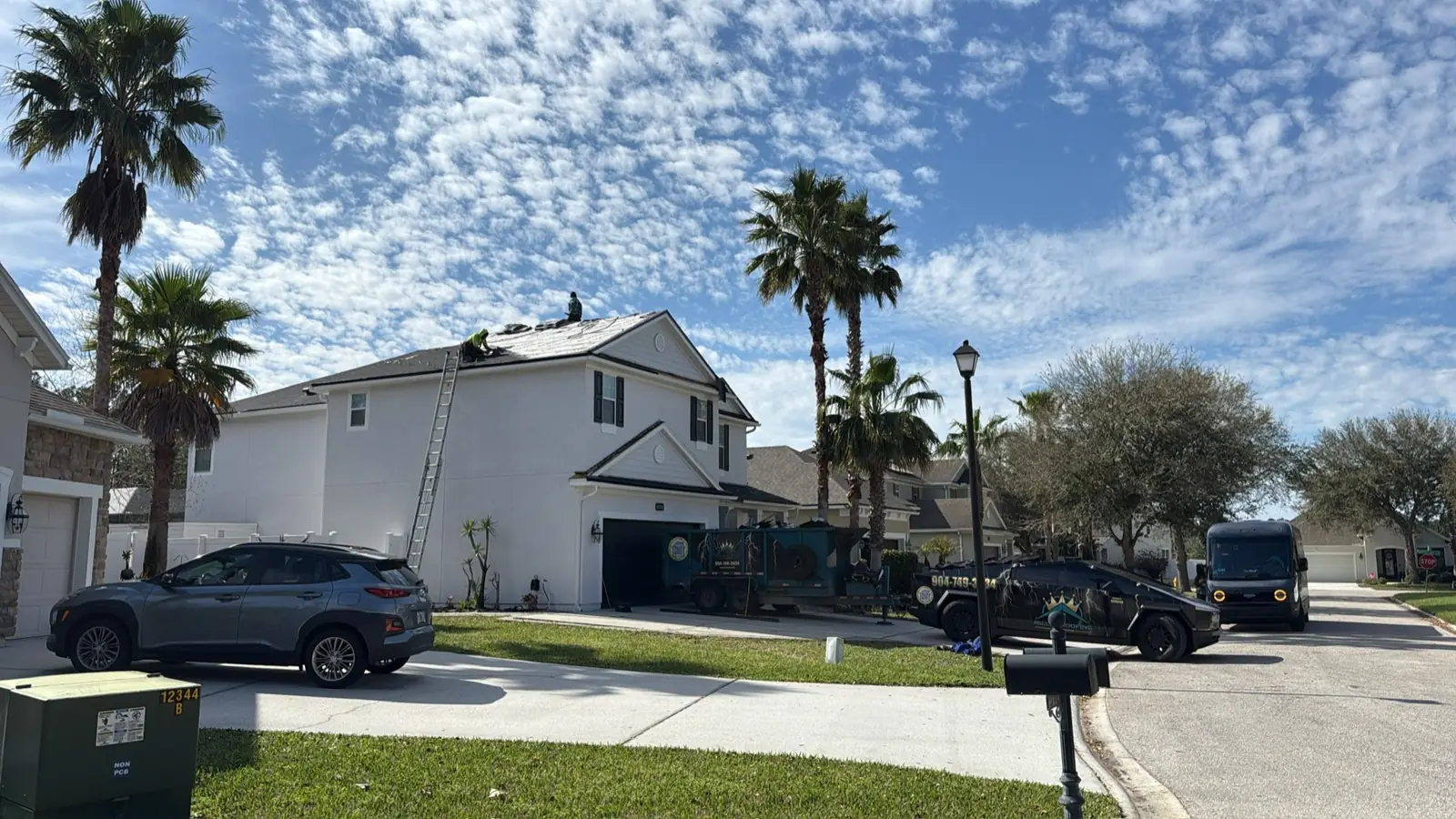 Crew on a two-story roof with the Miller Roofing wrapped truck and dump trailer parked in the driveway under a blue sky