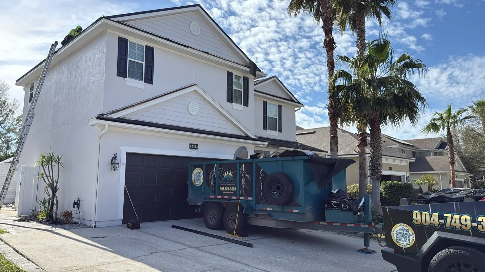 White two-story home with the Miller Roofing dump trailer and wrapped truck in the driveway
